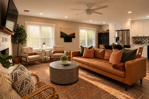 A living room with a sofa, chairs, a coffee table, and a kitchen area with cabinets and appliances.