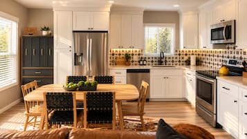 Une cuisine moderne avec des meubles blancs, des appareils en acier inoxydable et un coin repas comprenant une table et des chaises en bois.