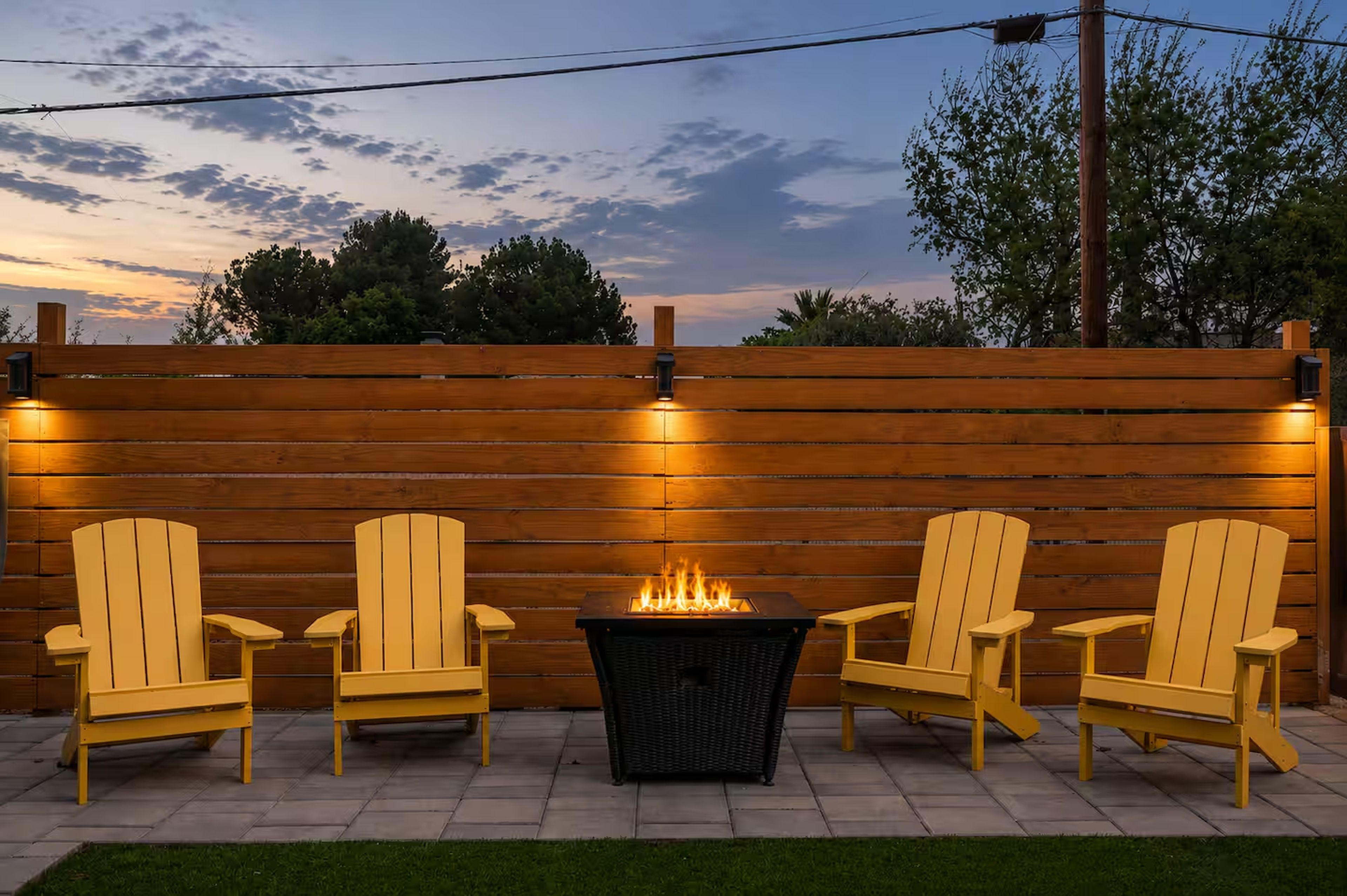 A patio with three Adirondack chairs, a fire pit, and a wooden fence.