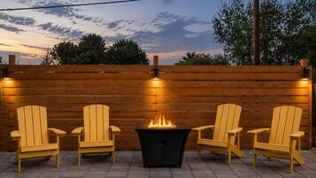 A patio with three Adirondack chairs, a fire pit, and a wooden fence.