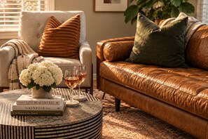 A cozy living room with a leather sofa, a round coffee table with books and a vase of flowers, and a side table with glasses of wine. - The Tipsy Moon-New Hot Tub-Beautiful Mid-Century Modern Home-20min to Sedona (Cottonwood)