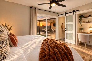 A bedroom with a bed, a desk, and a view of the outside.