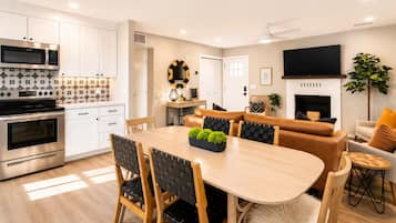 Una cucina moderna con elettrodomestici integrati, un'area pranzo con tavolo e sedie in legno e un soggiorno con divano e televisore a schermo piatto.
