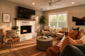 A living room with a fireplace, a sofa, a chair, a coffee table, and a ceiling fan. - The Tipsy Moon-New Hot Tub-Beautiful Mid-Century Modern Home-20min to Sedona (Cottonwood)