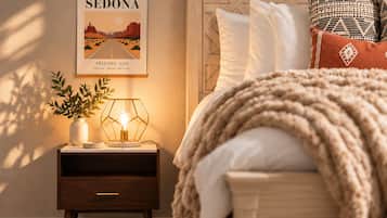 A bedroom with a bed, a nightstand with a lamp, a framed picture of Sedona, and a plant.