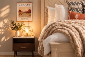 A bedroom with a bed, a nightstand with a lamp, a framed picture of Sedona, and a plant. - The Tipsy Moon-New Hot Tub-Beautiful Mid-Century Modern Home-20min to Sedona (Cottonwood)