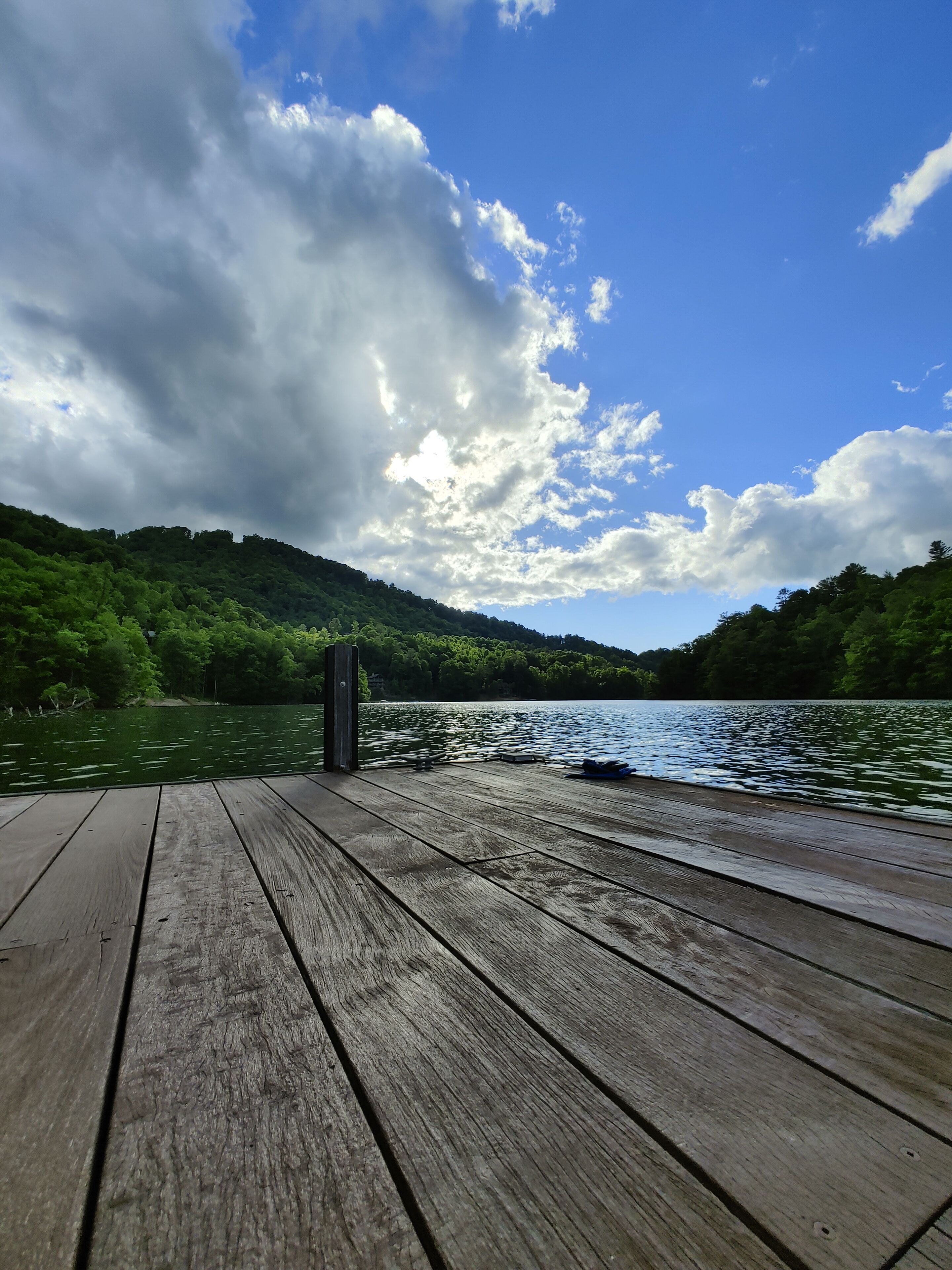 Eine Holzsteganlage, die sich in einen See erstreckt, mit einer bewaldeten Hügelkette im Hintergrund.