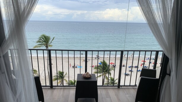 Un balcón con vista a la playa, una mesa con un cuenco y una silla.