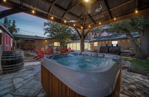 Ein Whirlpool unter einer Holzpergola mit Lichterketten, Steinböden und Gartenmöbeln.