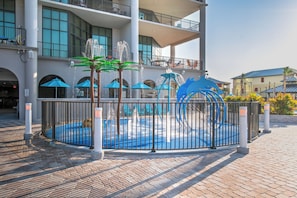A courtyard with a water feature, umbrellas, and a decorative sculpture.