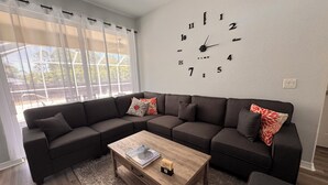 A modern living room with a sectional sofa, a wooden coffee table, and a wall clock.