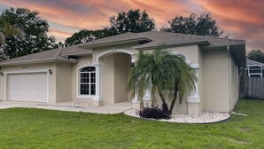 A single-story house with a garage, a large window, and a small palm tree in the front yard.