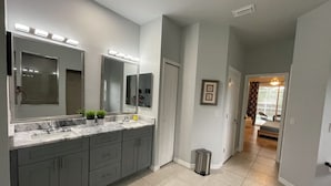 A modern bathroom with a double sink, large mirrors, and a trash can.
