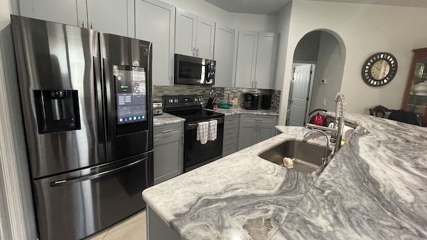 A modern kitchen with stainless steel appliances, a marble countertop, and light grey cabinetry.
