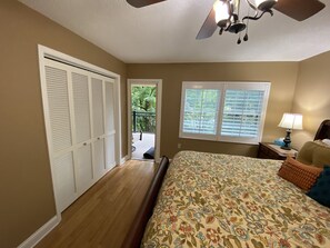 A bedroom with a bed, a ceiling fan, a window with blinds, a nightstand with a lamp, and a door leading to a balcony. - CREEKSIDE VIBES 2BR/2BA 1ST FLOOR, WALK TO GATLINBURG, -AUGUST SPECIAL! BOOK NOW (Gatlinburg)