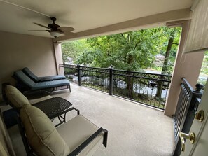 Ein Balkon mit zwei Liegestühlen, einem Deckenventilator und Blick auf einen Fluss und Grünflächen.