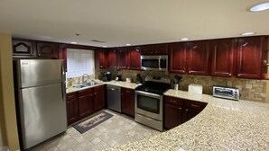 Uma cozinha com armários de madeira escura, eletrodomésticos de aço inoxidável, bancadas de granito e painel de azulejos.