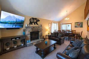 A living room with a fireplace, a television, a dining area, and a chandelier.