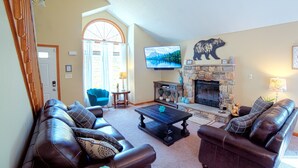 A living room with leather sofas, a stone fireplace, a television, and a large window with curtains.