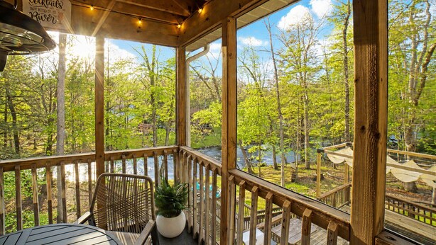 A wooden deck with a view of a river and trees, a sign for cocktails, and a table with chairs.