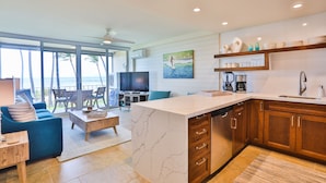 A modern kitchen with a marble island, wooden cabinets, and a large window overlooking the ocean. - Exceptionally Remodeled Oceanfront, Sunsets,  A/C, King bed Hale Kai O Kihei (Kihei)