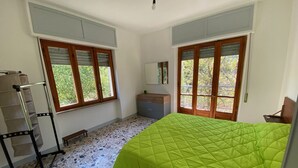 Ein Schlafzimmer mit einer grün gesteppten Bettdecke, einer Holzbank, einem kleinen Tisch und einem Spiegel an der Wand.