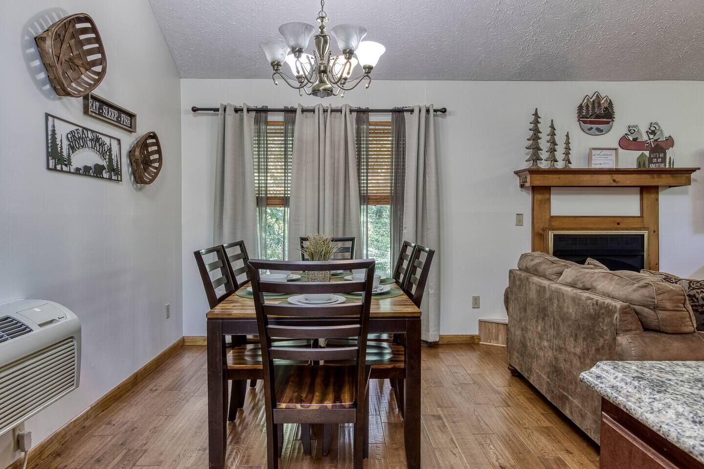 A dining area with a wooden table and chairs, a chandelier, and a fireplace with decorative items.