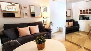 A modern living room with a black sofa, a round dining table, and a kitchen area visible through a glass partition. - Wonderful Studio in Marbella Centre on the Second Line Beach (Marbella)