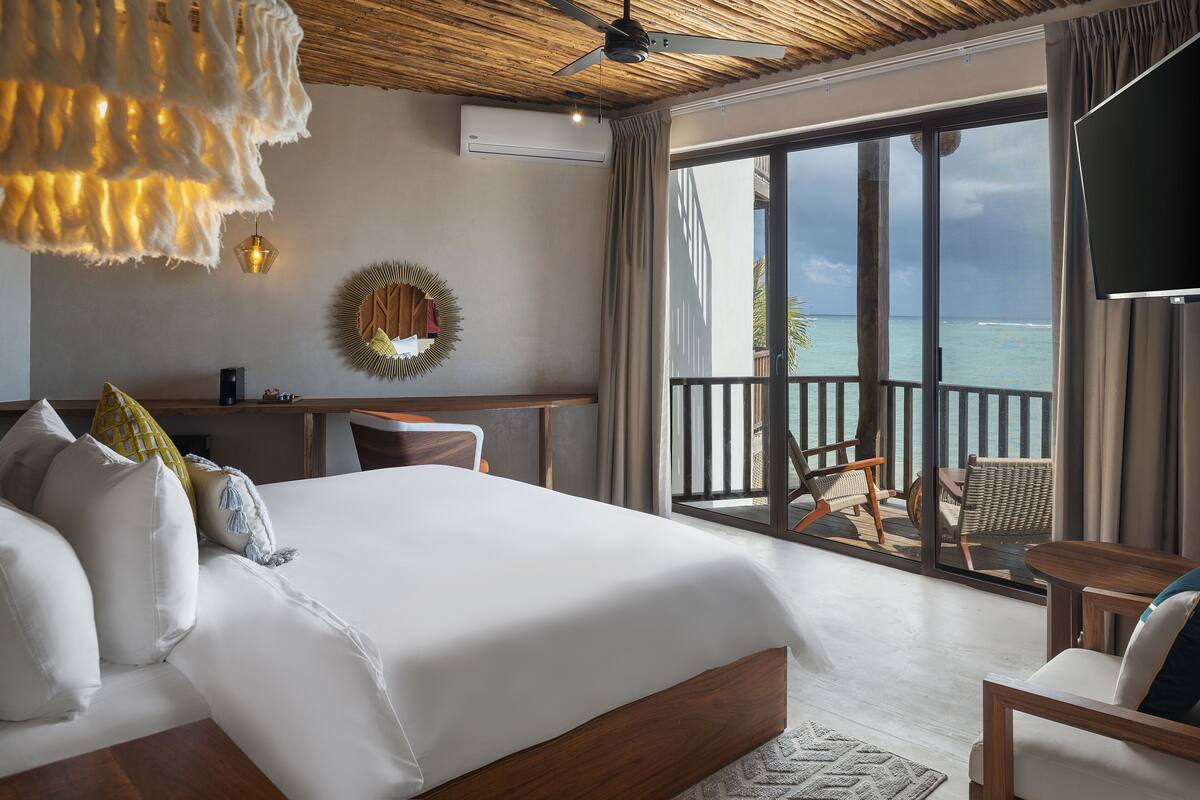 A bedroom with a large bed, a desk, and a view of the ocean through a sliding glass door.