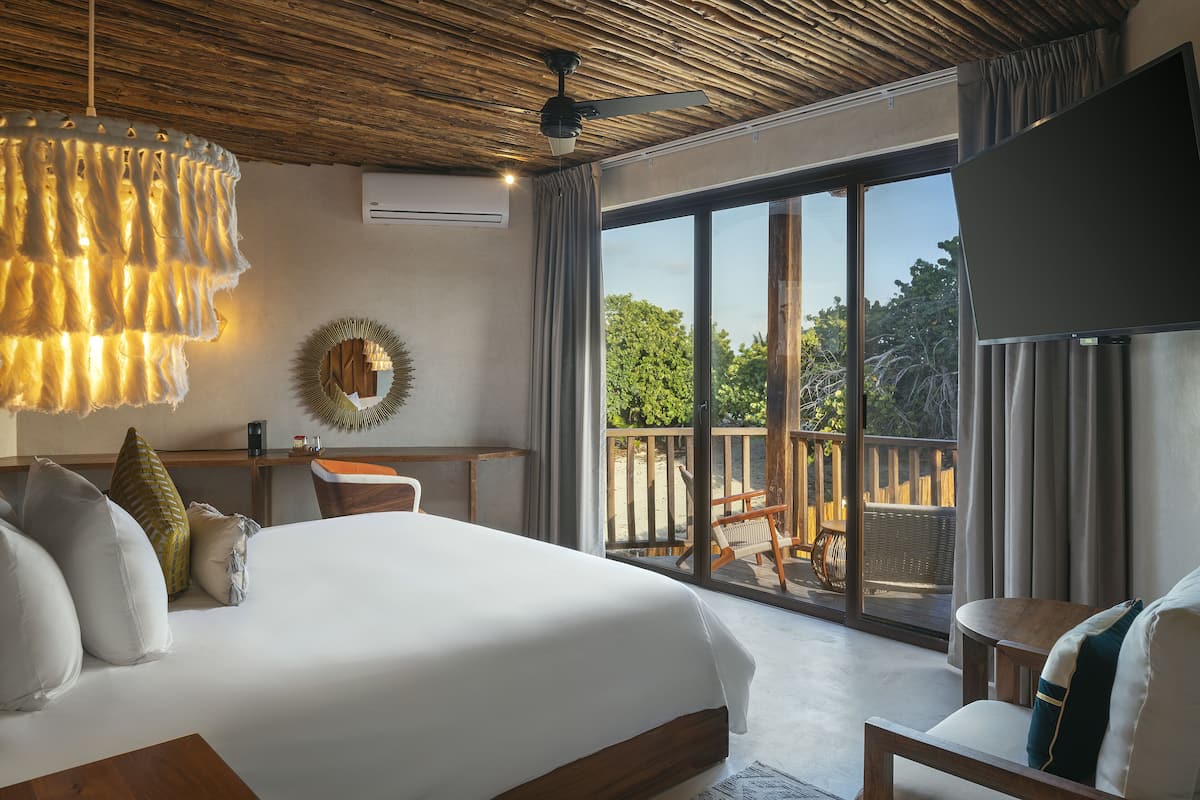 A bedroom with a large bed, a ceiling fan, a TV, and a balcony with outdoor furniture.