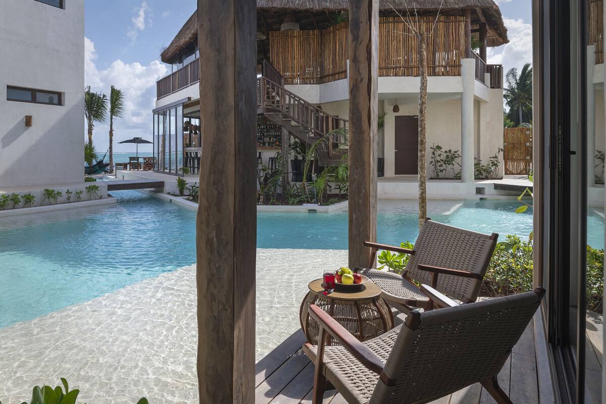 A poolside area with wicker chairs, a small table with fruit and a drink, and a view of the pool and ocean.