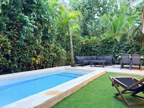 A swimming pool surrounded by lush greenery, a wooden deck, and outdoor furniture.