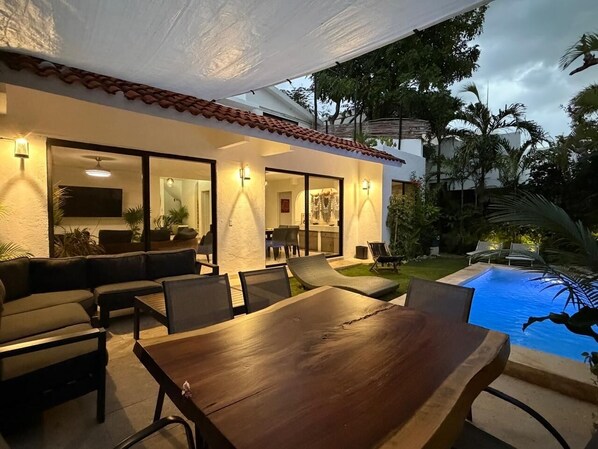 An outdoor patio with a dining table and chairs, a sofa, and a pool.