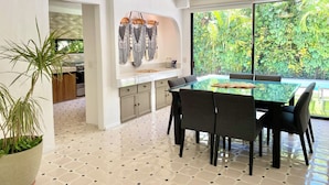 Cocina moderna con comedor que incluye una mesa y sillas de vidrio, ventilador de techo y vistas a exuberante vegetación.