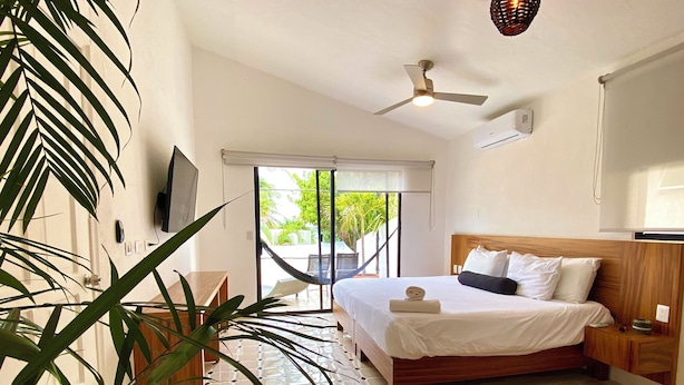 Un dormitorio con cama, ventilador de techo, televisor y vistas al exterior.