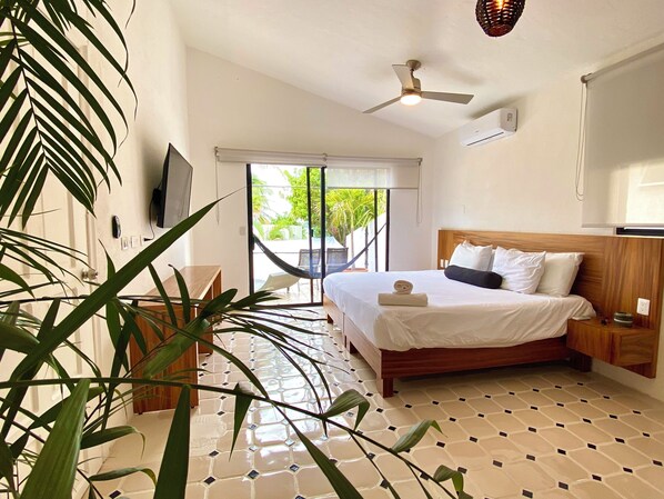 A bedroom with a bed, a ceiling fan, a TV, and a view of the outdoors.