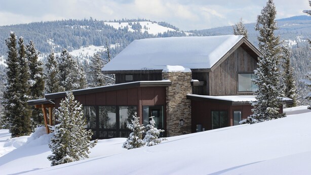 Een modern ski-resort lodge met een gevel van steen en hout, grote ramen en uitzicht op besneeuwde bergen.