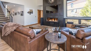 Een moderne woonkamer met leren banken, een open haard en een groot raam met uitzicht op een achtertuin.