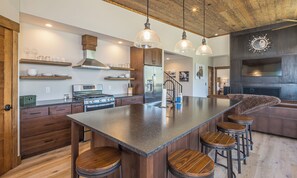 A modern kitchen with wooden cabinetry, a central island with stools, stainless steel appliances, and pendant lighting.