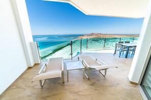 Een balkon met twee comfortabele stoelen en een tafel, met uitzicht op een strand en turquoise water.