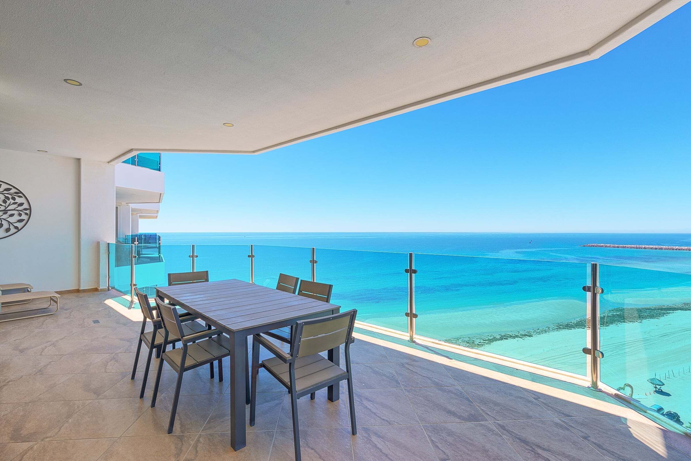 Een balkon met een tafel en stoelen, uitkijkend op een heldere blauwe zee en een verre kustlijn.