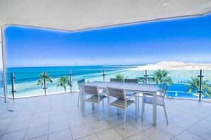 Une terrasse avec une table et des chaises, donnant sur une plage et l’océan.
