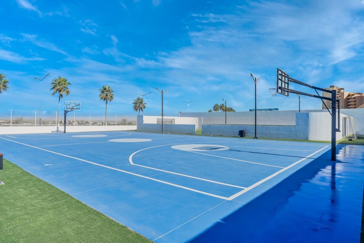 Ein Basketballplatz mit blauer Spielfläche, Palmen und blauem Himmel.