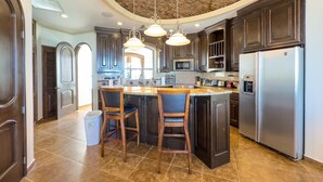 A spacious kitchen with dark wood cabinets, a central island with bar stools, stainless steel appliances, and a brick ceiling. - Esmeralda Beach Resort 2 Bedrooms Condo A 203 (Puerto Peñasco)