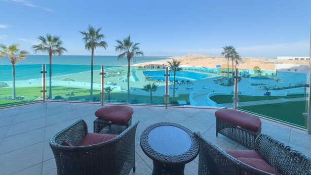 A balcony with wicker furniture, a pool, and a view of the beach and ocean. - Esmeralda Beach Resort 2 Bedrooms Condo A 203 (Puerto Peñasco)