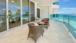 A balcony with wicker furniture and a glass door leading to a pool area. - Esmeralda Beach Resort 2 Bedrooms Condo A 203 (Puerto Peñasco)