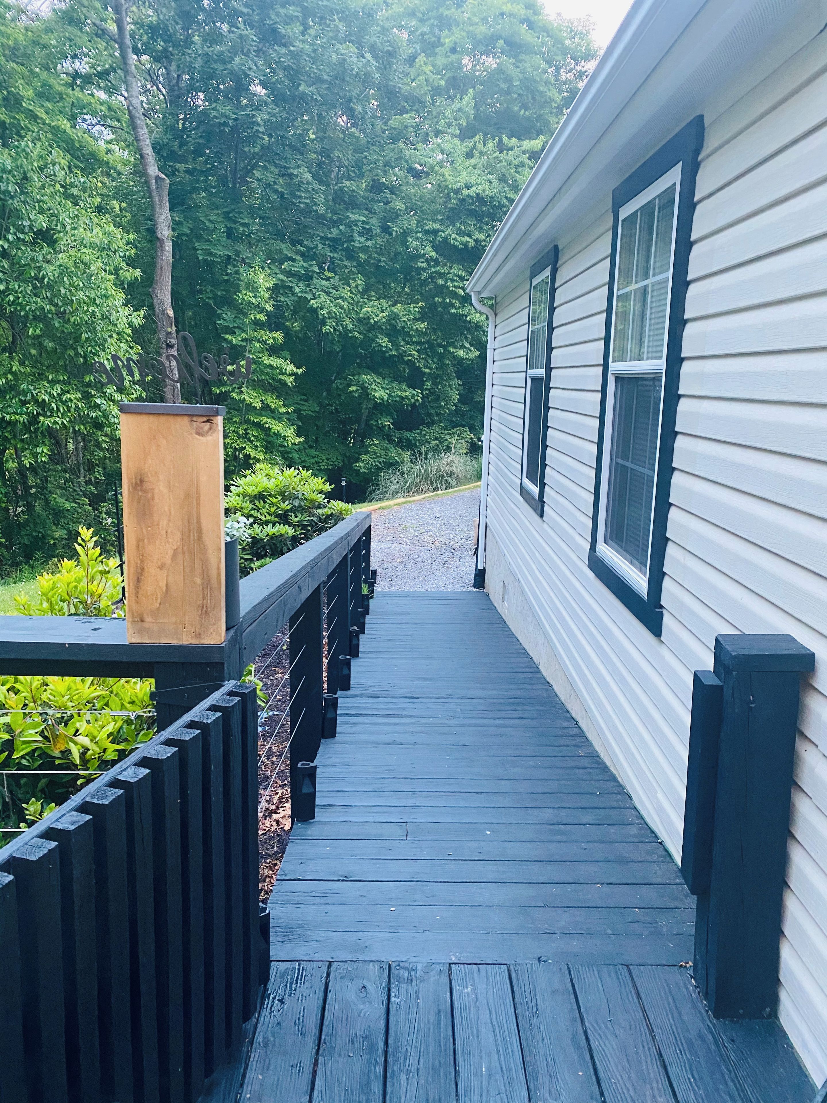 Une terrasse en bois menant à une maison dotée d’une rambarde sombre et d’une boîte aux lettres.
