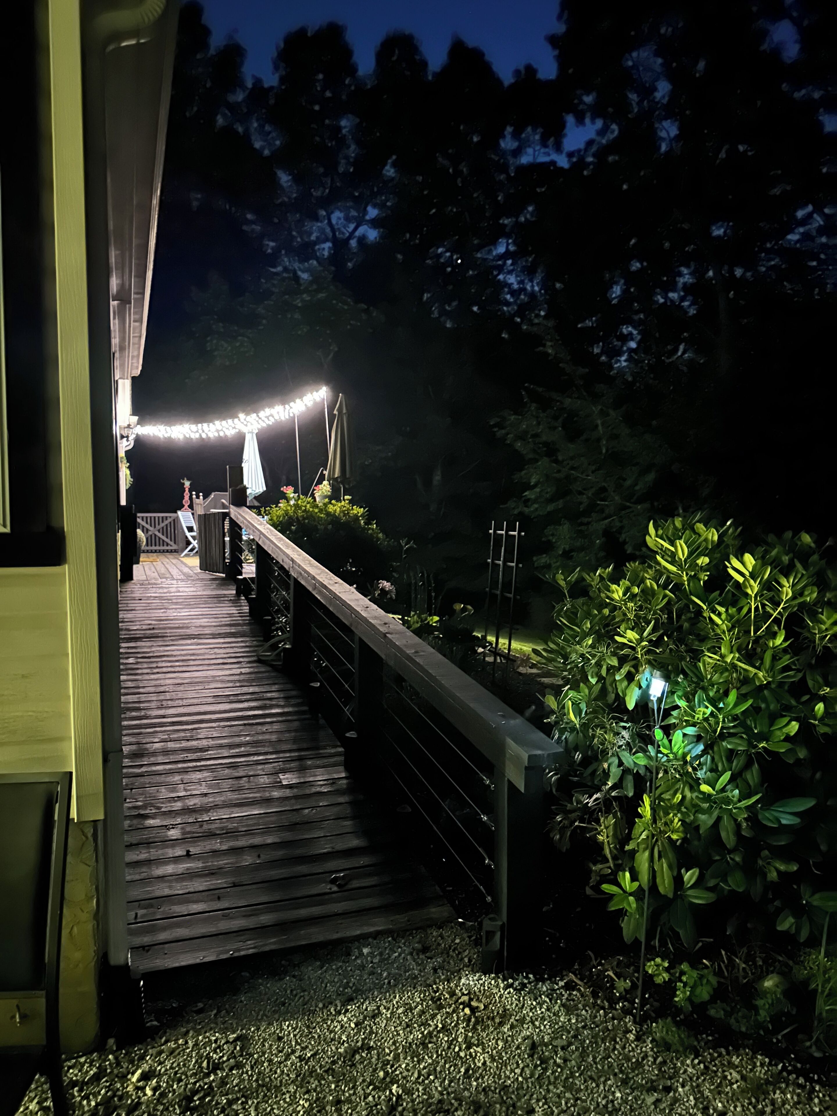 A wooden deck leading to a building with string lights overhead.