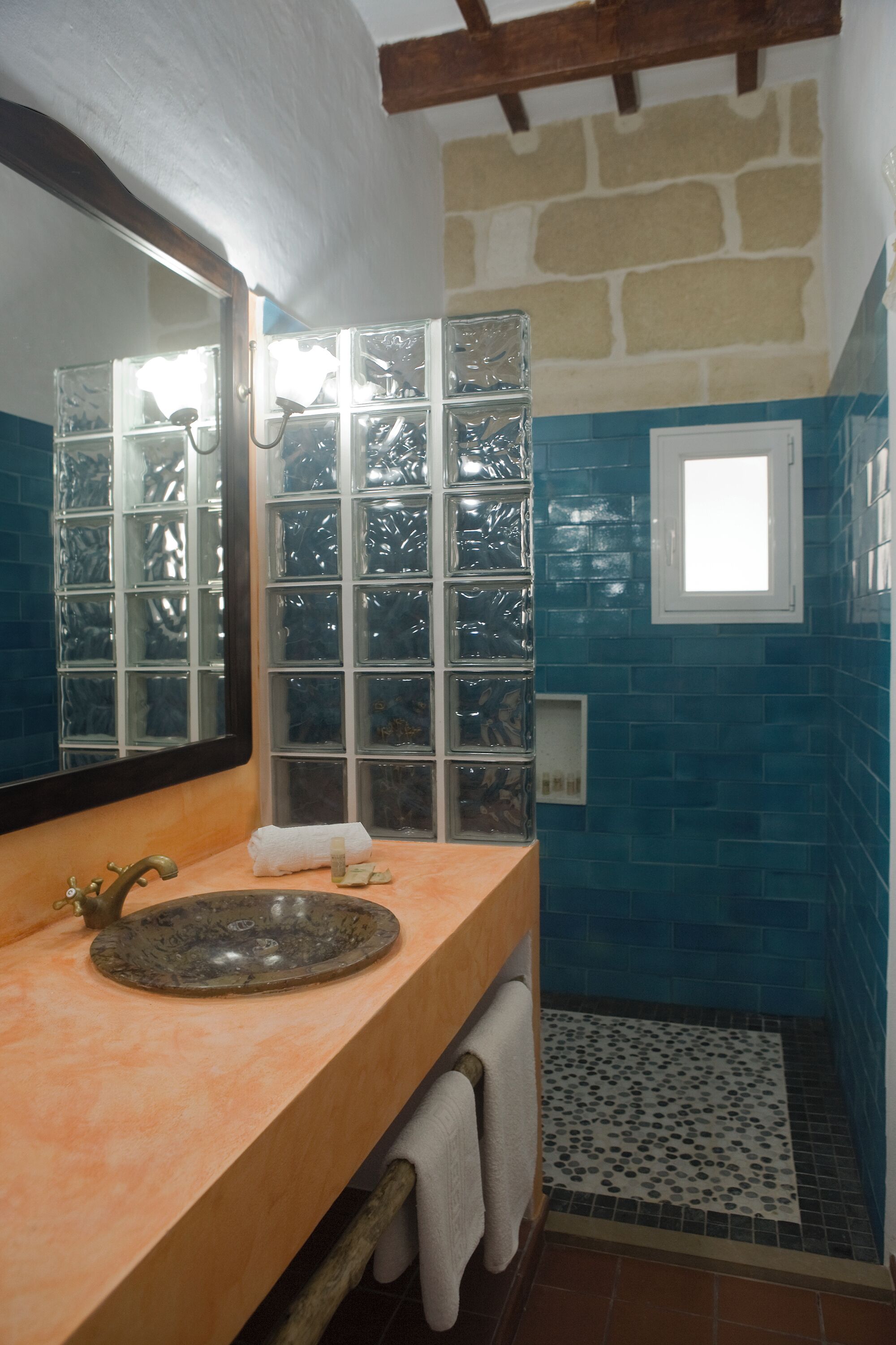 A bathroom with a stone wall, a blue-tiled shower area, a wooden vanity with a sink, and a large mirror.