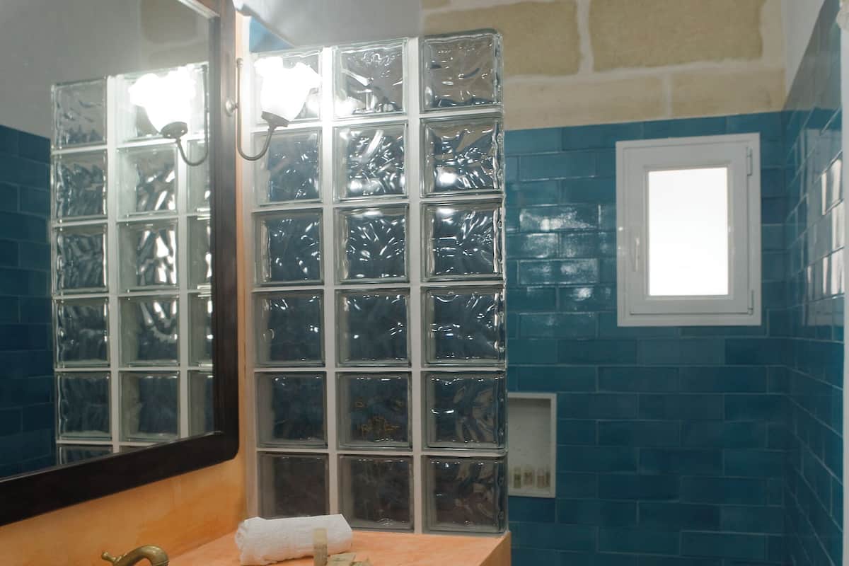 A bathroom with a stone wall, a blue tiled shower area, and a wooden vanity with a sink.